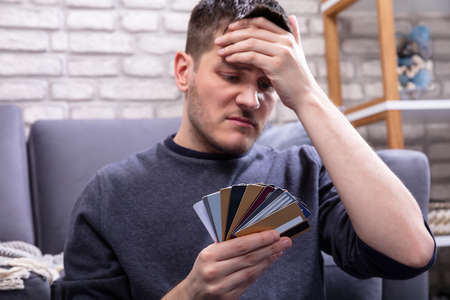 Stressed Man Looking At Too Many Credit Cards In Home