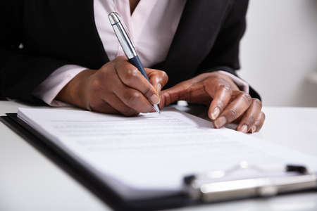 Close-up Of Businesswoman's Hand Signing On Papers Over Deskの写真素材