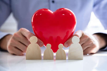 Person's hand protecting red heart with family figuresの写真素材