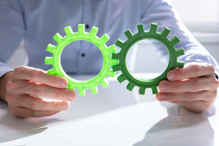 Businessman Joining Together Gears On Wooden Table At Workplace