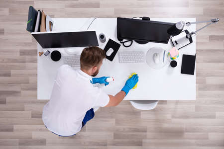 Janitor cleaning white desk in modern office