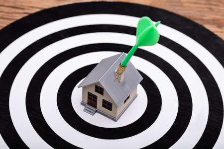 Close-up Of Green Dart Arrow Hitting House Model On Dartboardの写真素材