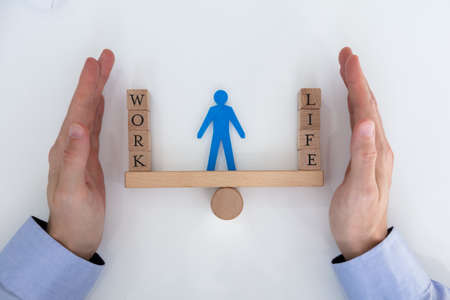 Close-up Of A Businessman's Hands Covering Balance Between Life And Work On Seesawの写真素材