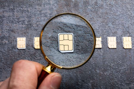 Person's Hand Holding Magnifying Glass Over Nano Sim Card On Rough Backgroundの写真素材