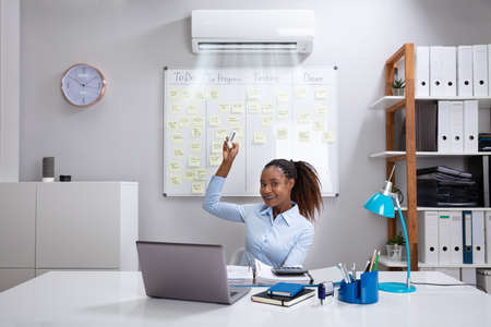 Young Businesswoman Operating Air Conditioner With Remote Controller In Officeの写真素材