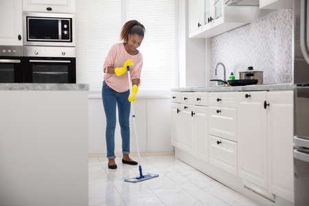 Smiling Female Janitor Cleaning White Floor With Mop In The Kitchenの写真素材