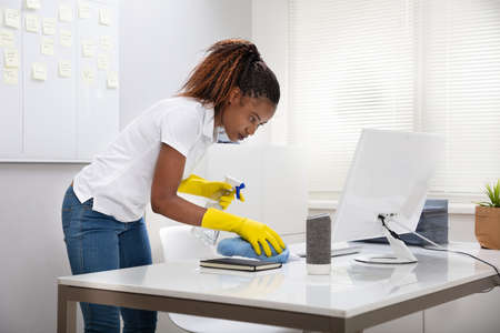 Young Female Janitor Cleaning Desk With Napkin In Officeの写真素材