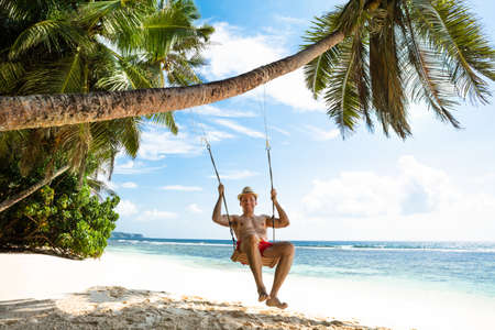 Happy Young Man Enjoying Swinging On The Idyllic Beachの写真素材