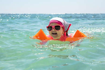 Laughing Girl Toddler Wearing Sunglasses And Inflatable Armbands Swimming In The Sea
