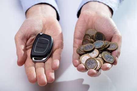 An Elevated View Of Man's Hand Holding Black Car Key And Golden Coins