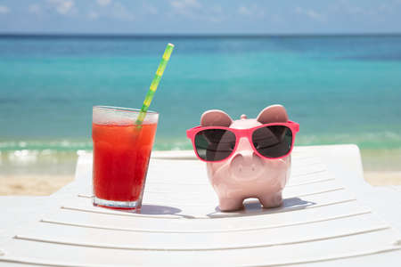 Close-up Of Fresh Juice And Piggybank With Sunglasses On White Deck Chair At Beachの写真素材