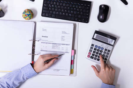 An Elevated View Of Businessman's Hand Using Calculator While Calculating Invoice On Deskの写真素材
