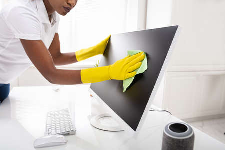 Close-up Of A Woman's Hand Cleaning Desktop Screen With Green Rag In Office