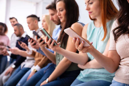 Multi-ethnic Young People Leaning Near Table In Row Using Smartphone