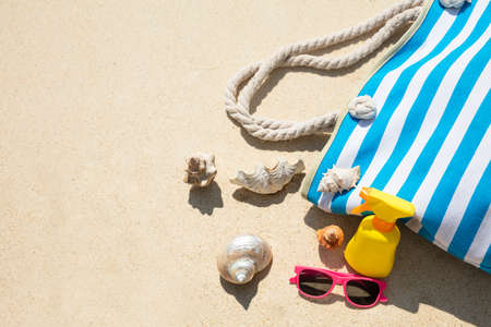 Seashells, Sunglasses, Sunscreen Bottle And Handbag On Sand At Beach