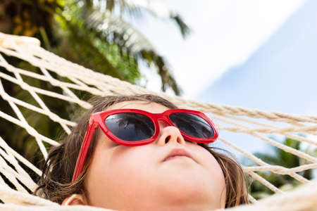 Close-up Of A Girl Wearing Red Sunglasses Lying On Hammockの写真素材