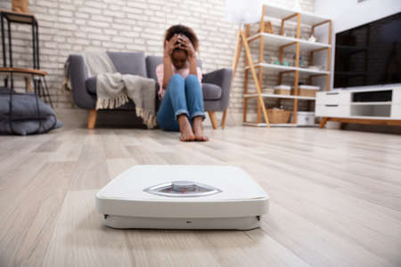 Close-up Of A Weighing Scale In Front Of Upset Woman