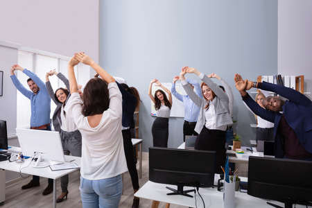 Happy Multi-ethnic Businesspeople Raising Hands Doing Stretching Exercise In Officeの写真素材