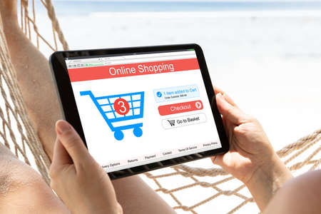 Close-up Of Woman Shopping Online On Digital Tablet Lying On Hammock At Beachの写真素材