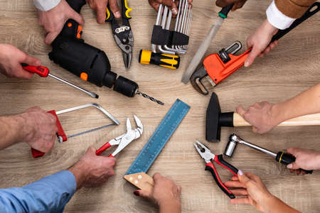 Top View Of People's Hand Holding Carpentry Tools Over Wooden Deskの写真素材