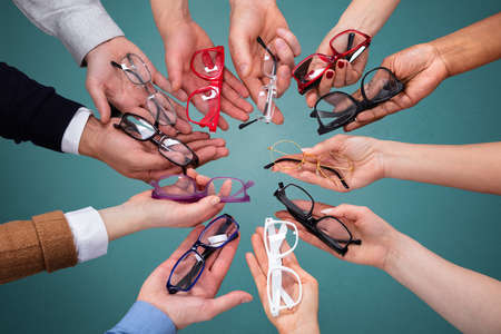 Top View Of People's Hand Showing Variety Of Spectacles Against Green Backdropの写真素材