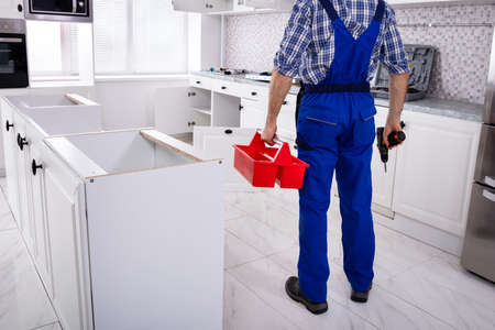 Rear View Of A Repairman In Uniform Holding Tool Box Installing Kitchen Induction Ceramic Hobの写真素材