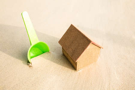 Green Plastic Shovel And Miniature House Model On Sandy Beach