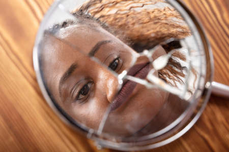 Close-up Of Young Woman Looking At His Face In A Broken Mirrorの写真素材