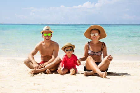 Portrait Of A Happy Family Wearing Sunglasses Sitting On Sand At Beachの写真素材