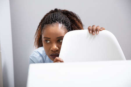 Afraid African Businesswoman Peeking Behind Chair In Office