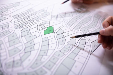 Close-up Of Human Hand Holding Pencil Over Paper Cadastre Map