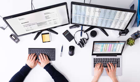 Elevated View Of Businesspeople's Hand Checking Invoice On Computer Over White Deskの写真素材