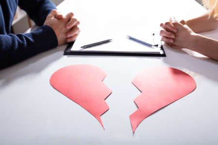 Couple's Hand With Divorce Paper And Broken Red Heart Over White Deskの写真素材