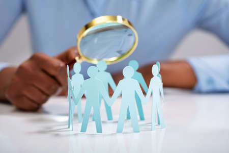 Close-up Of Businessperson Holding Magnifying Glass Over The Human Figures Forming Circleの写真素材