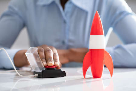 Businesswoman's Hand Launching Rocket By Pressing Red Buttonの写真素材