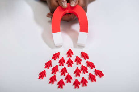 Close-up Of A Person's Hand Holding Red Horseshoe Magnet Attracting Red Human Figuresの写真素材