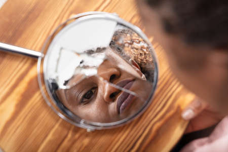 Close-up Of Young Woman Looking At His Face In A Broken Mirrorの写真素材