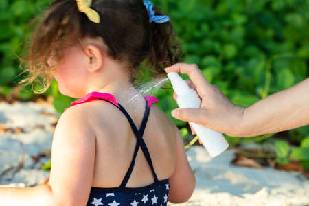 Close-up Of Woman's Hand Spraying Lotion On Her Daughter's Backの写真素材