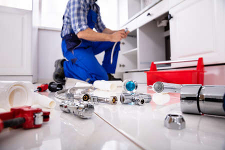 Plumber Tools And Equipment On Floor In Kitchen With Plumber Installing The Sink At Backgroundの写真素材