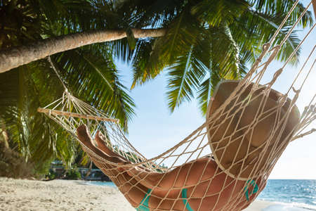 Close-up Of A Woman In Bikini Wearing Hat Lying On Hammock At Beachの写真素材