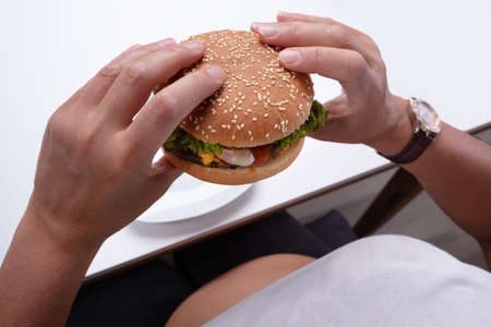 An Overhead View Of An Overweight Woman Holding Hamburger In Hand