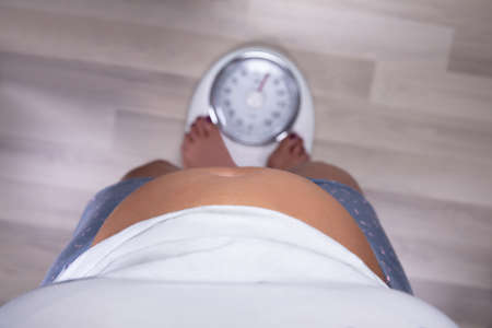 An Elevated View Of A Overweight Woman Standing On The Scale Over Hardwood Floor