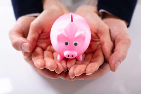 Elevated View Of Pink Piggybank On Palm Of Couple's Hand Over White Desk