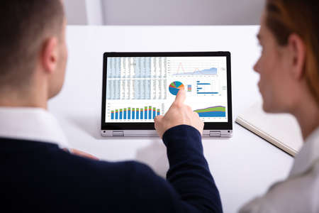 Rear View Of Businessman's Hand Pointing Laptop Screen Showing Bar Graph Over White Desk