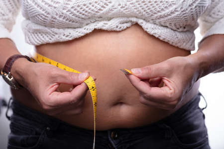 Midsection Of Woman Measuring Her Belly With Yellow Measuring Tape