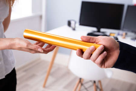 Businessman's Hand Passing Golden Relay Baton To His Female Partner
