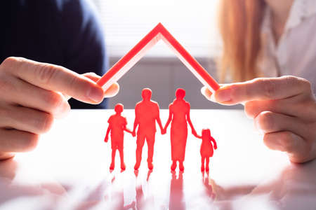 Close-up Of A Person's Hand Protecting Family Figures With Red Roofの写真素材
