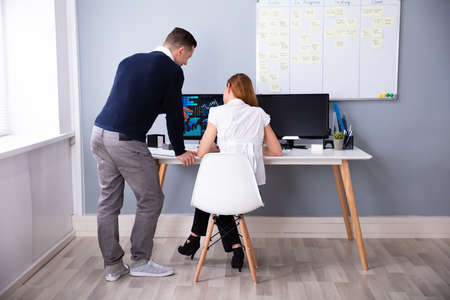 Rear View Of Two Businesspeople Analyzing Graph On Computer Screen In Officeの写真素材