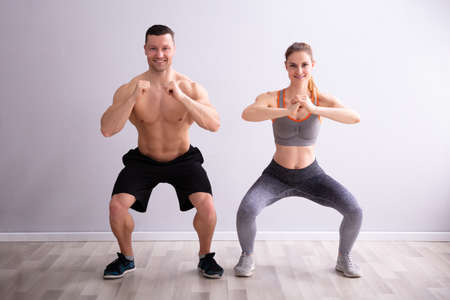 Side View Of Happy Fitness Couple In Sportswear Doing Squat Exercises At Gymの写真素材