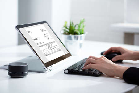 Close-up Of Businesswoman's Hands Working On Invoice On Laptop At Office